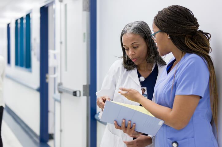 nurse and doctor discussing file in hospital hallway nurse and doctor discussing file in hospital hallway