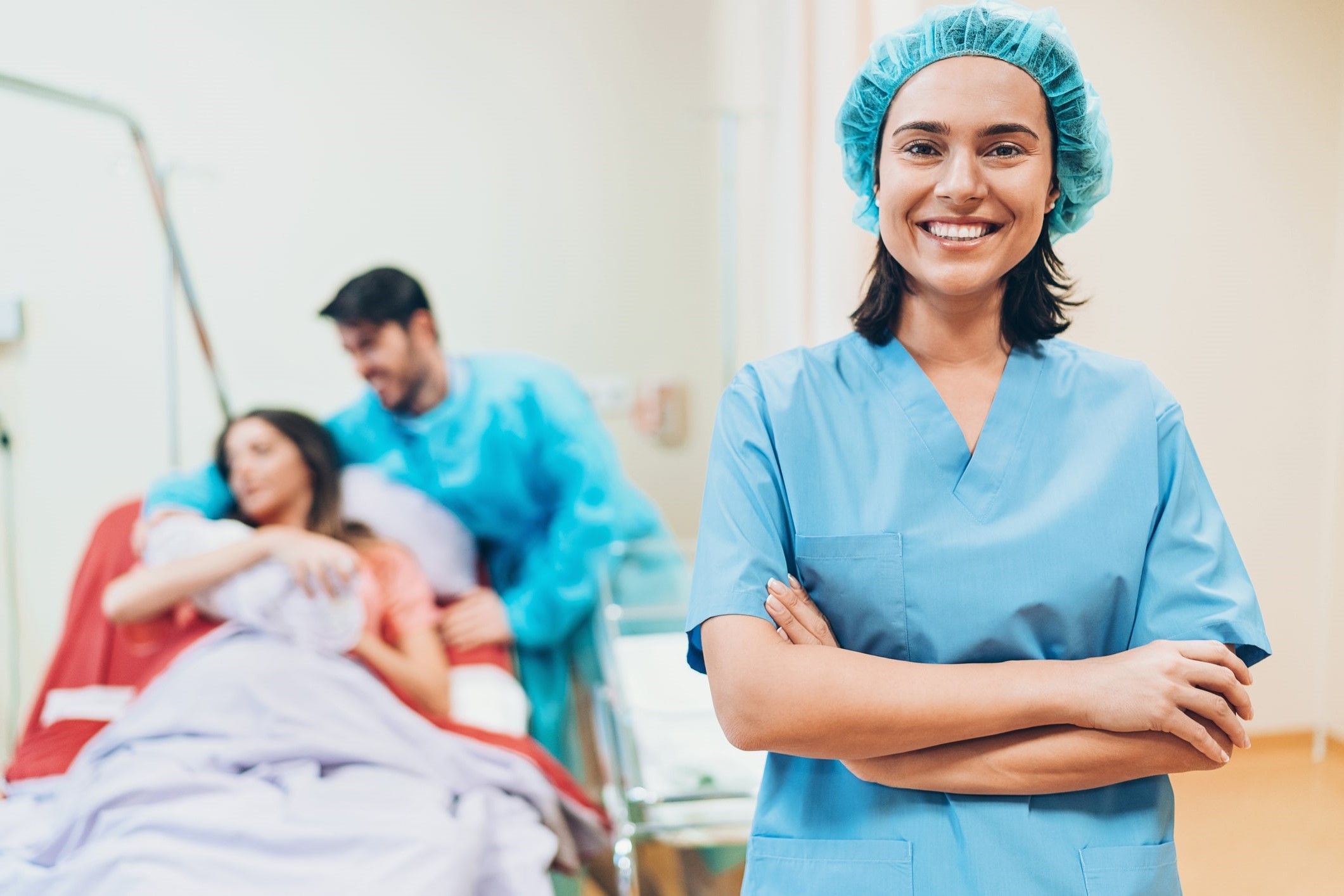 smiling labor and delivery travel nurse stands in front of new parents and baby smiling labor and delivery travel nurse stands in front of new parents and baby