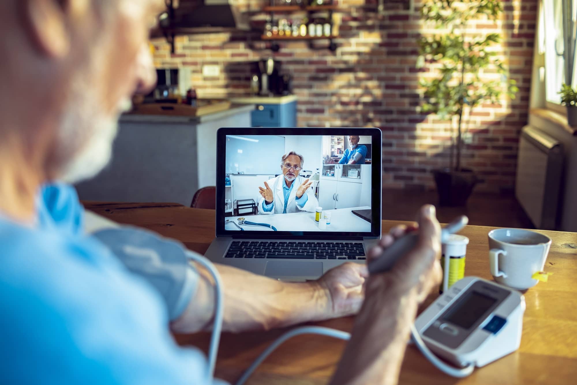 telehealth appointment with doctor visible on computer and patient at home using blood pressure cuff telehealth appointment with doctor visible on computer and patient at home using blood pressure cuff