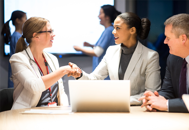 Female physician shaking hands with business woman at table Female physician shaking hands with business woman at table