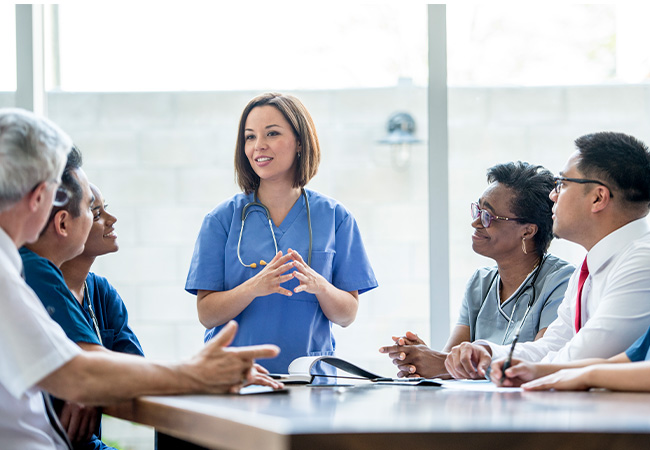 Female physician talking to seated group of people in office meeting Female physician talking to seated group of people in office meeting